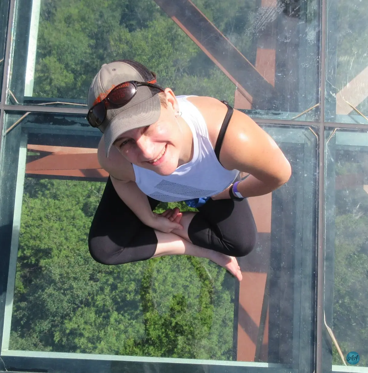 Personne assise en tailleur sur une passerelle vitrée suspendue au-dessus une forêt